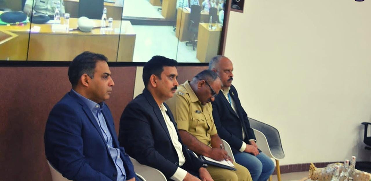 Senior officials and a police officer seated at an official review meeting in a conference room.